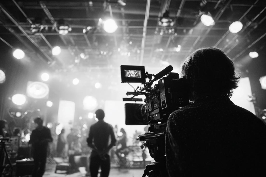 Ultrarealistyczne, szerokie ujęcie profesjonalnego planu filmowego w trakcie pracy. W centrum znajduje się operator z kamerą filmową, a obok niego reżyser obserwujący scenę z aktorami w tle.