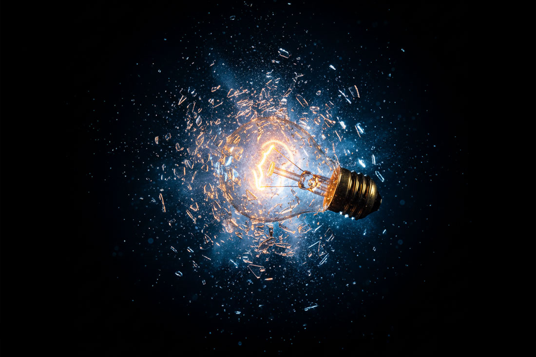 Eksplozja żar&oacute;wki uchwycona w technice slow motion na czarnym tle, ukazująca zamrożone w ruchu odłamki szkła i detale niewidoczne gołym okiem.